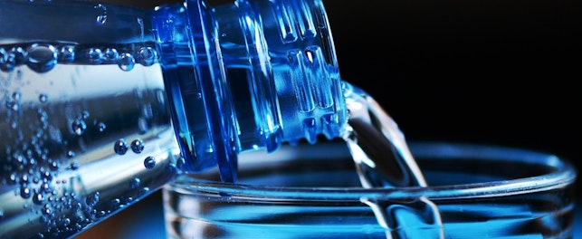 Zdjęcie przedstawia z bliska nalewanie wody do szklanki z plastikowej butelki.